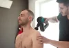 Zastosowanie fali uderzeniowej w leczeniu bólu mięśni Fizjoterapeuta wykonuje zabieg urządzeniem na barku siedzącego mężczyzny.