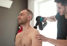 Zastosowanie fali uderzeniowej w leczeniu bólu mięśni Fizjoterapeuta wykonuje zabieg urządzeniem na barku siedzącego mężczyzny.