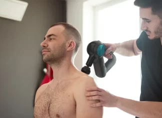 Zastosowanie fali uderzeniowej w leczeniu bólu mięśni Fizjoterapeuta wykonuje zabieg urządzeniem na barku siedzącego mężczyzny.