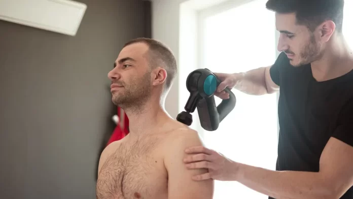 terapia-fala-uderzeniowa-bark Fizjoterapeuta wykonuje zabieg urządzeniem na barku siedzącego mężczyzny.